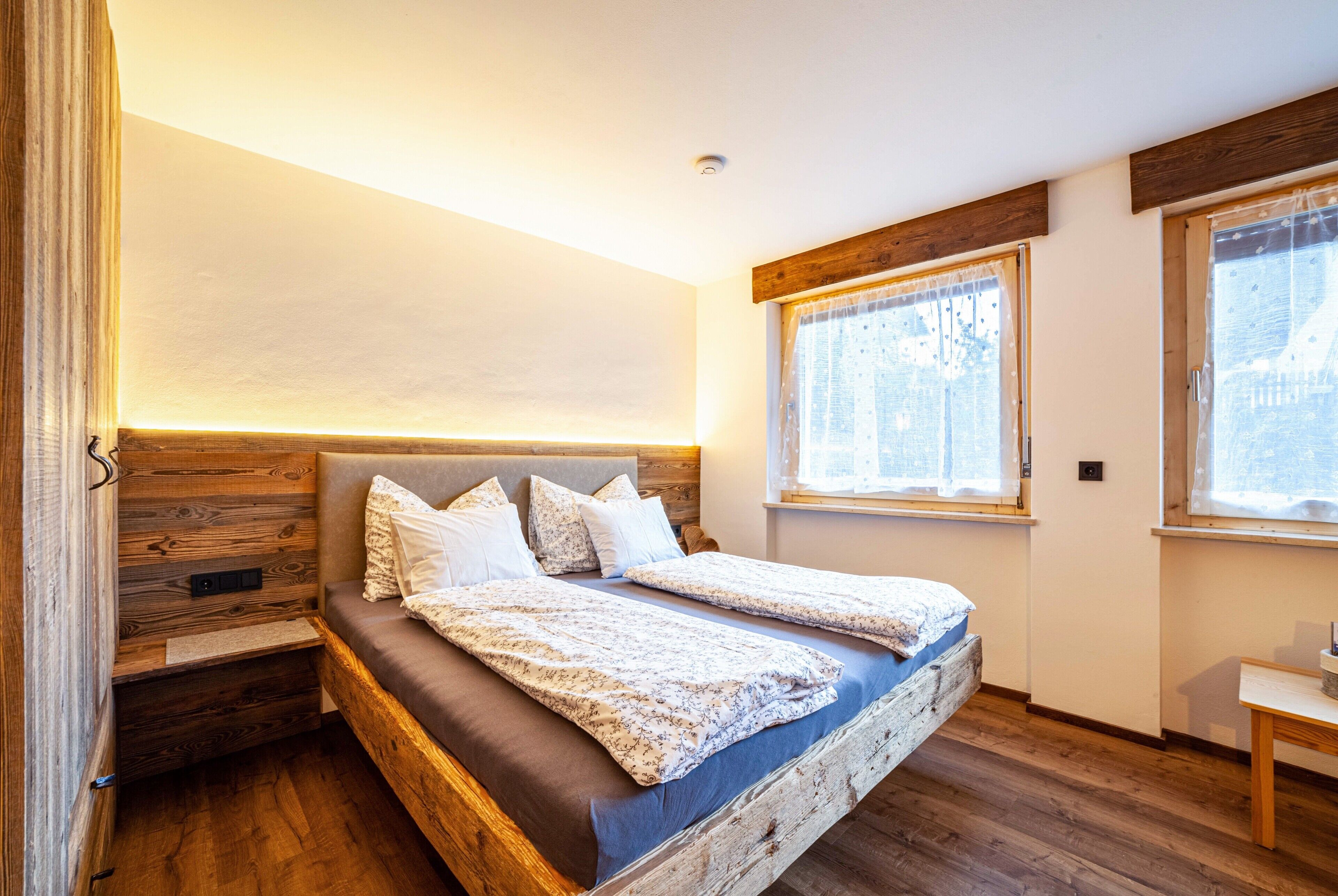 Un dormitorio con cabecera de madera, cama con colcha estampada y ventana con cortinas.