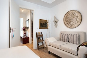 Ein Zimmer mit einer Couch, einem kleinen Holznachttisch, einer Wanddekoration und einem gerahmten Bild.