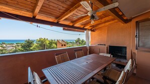 A wooden balcony with a table and chairs, a ceiling fan, and a view of the ocean. - Holiday Home 'Bianca' with Sea View, Private Terrace and Air Conditioning (Costa Rei)