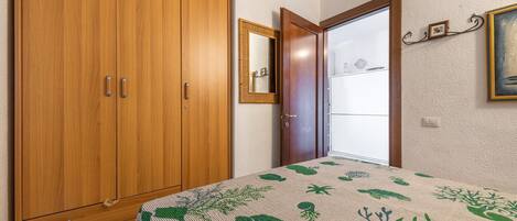 Un dormitorio con un armario de madera, una cama con colcha estampada, un espejo y una puerta que da a otra habitación.
