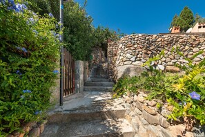 Un escalier en pierre menant à un bâtiment, entouré de verdure et surplombé d’un ciel bleu clair.