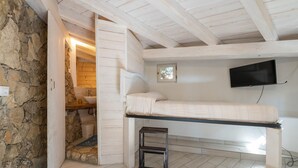 A bedroom with a bunk bed, a small stool, a stone wall, a wooden shelf, and a TV mounted on the wall. - Holiday Home 'Bianca' with Sea View, Private Terrace and Air Conditioning (Costa Rei)
