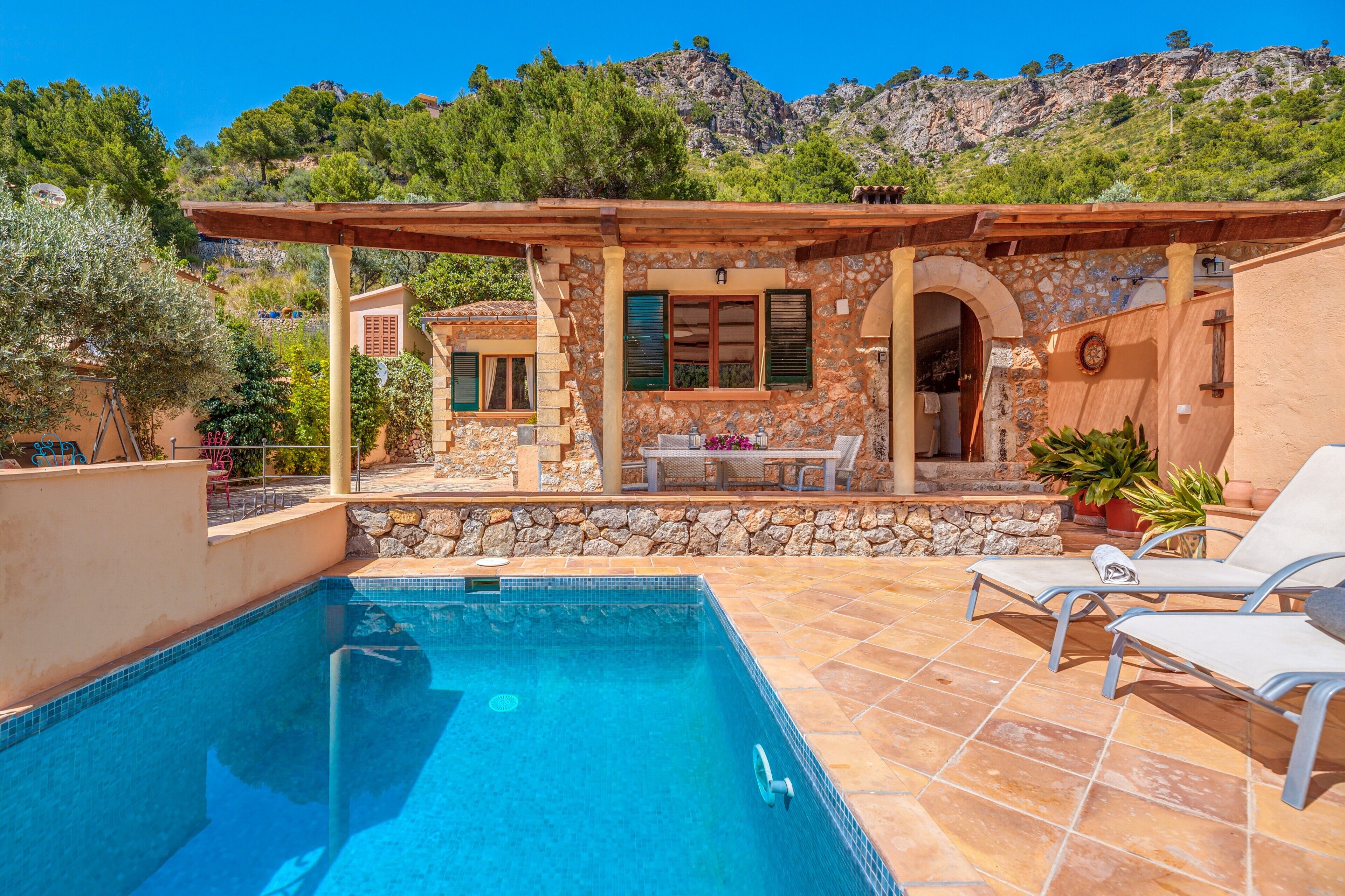A pool area with a stone wall, a pergola, and a view of the mountains.