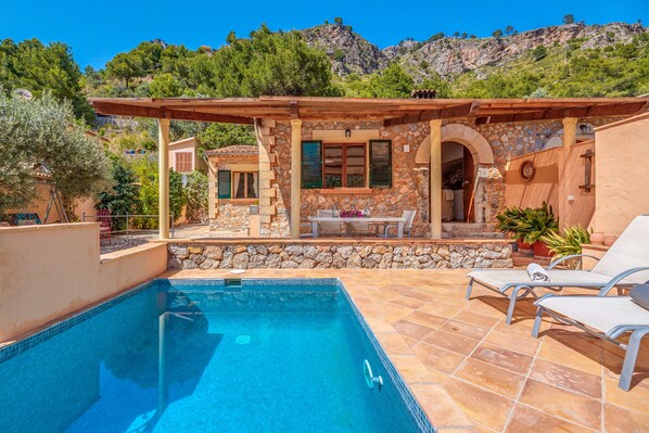 A pool area with a stone wall, a pergola, and a view of the mountains.