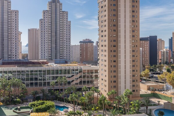 A high-rise building with a modern glass facade, surrounded by palm trees and a swimming pool.