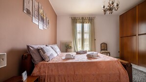 A bedroom with a bed, a nightstand, a chair, a radiator, and a wardrobe.
