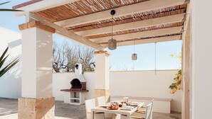 Eine Terrasse im Freien mit Tisch und Stühlen, einem Backofen aus Ziegeln und einer Pergola.