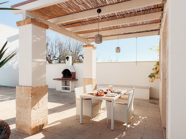 Une terrasse extérieure avec une table et des chaises, un four en briques et une pergola.