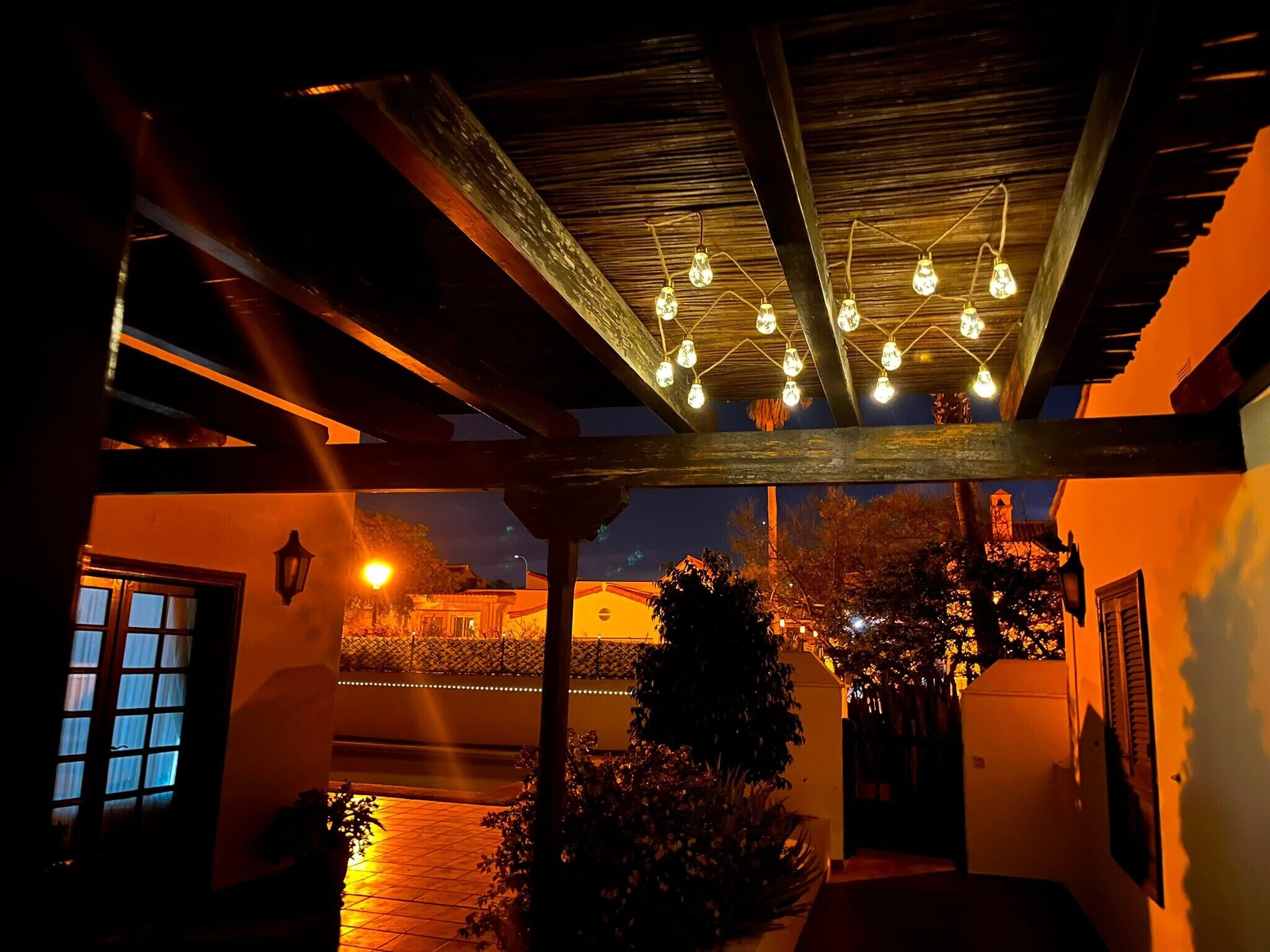 Un'area esterna coperta con soffitto in legno, lampade a sospensione e vista su un edificio sullo sfondo.