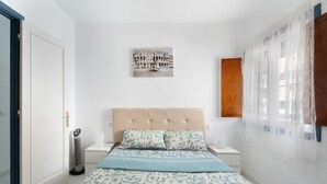 A bedroom with a bed, a wall-mounted picture, a bedside table, a nightstand, a window with sheer curtains, and a door. - 2-Bedroom Apartment on Los Cristianos Beach with Promenade Views (Los Cristianos)