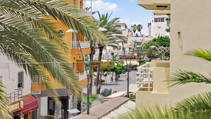 A street view with buildings, palm trees, and a sign for 'Bahia.' - 2-Bedroom Apartment on Los Cristianos Beach with Promenade Views (Los Cristianos)