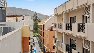 A narrow urban street with multi-story buildings, balconies, and a mountain in the background.