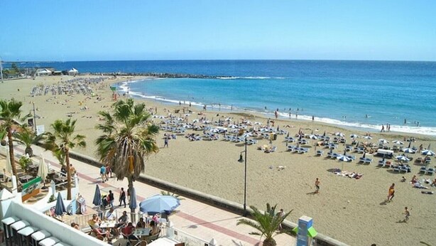 A beach with umbrellas and sun loungers, a clear sky, and a calm sea. - 2-Bedroom Apartment on Los Cristianos Beach with Promenade Views (Los Cristianos)