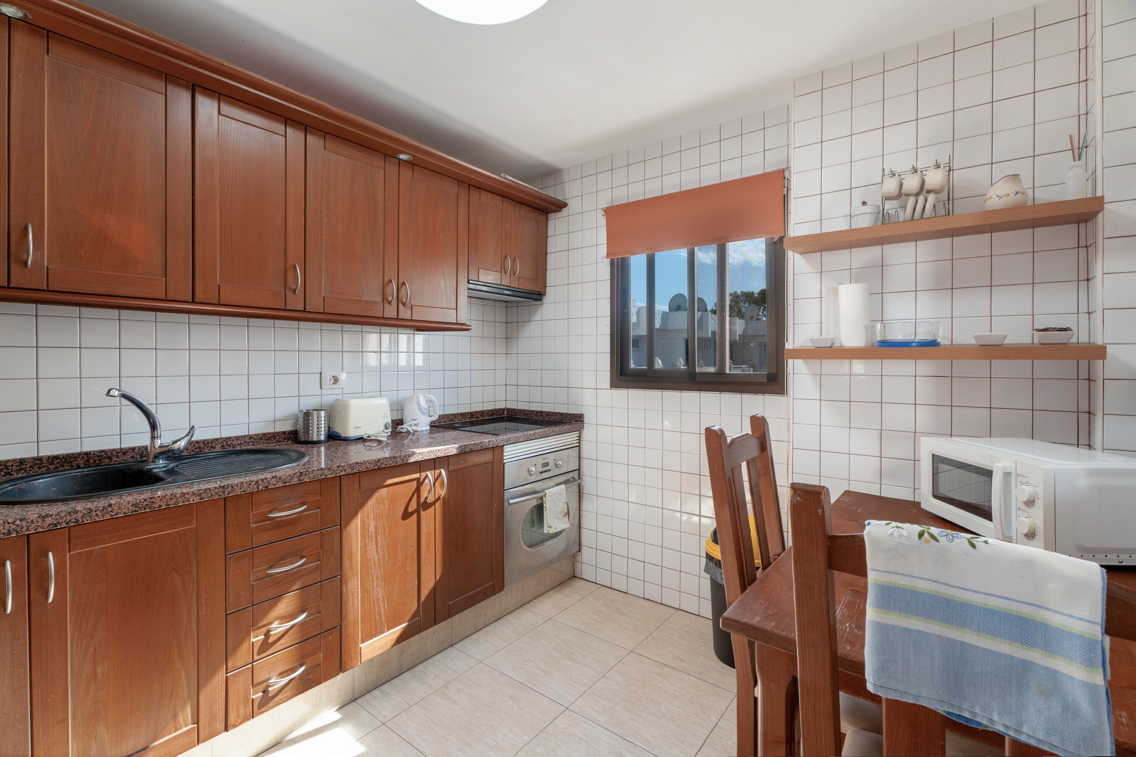 A kitchen with wooden cabinets, a sink, a stove, a microwave, and a window with a view.