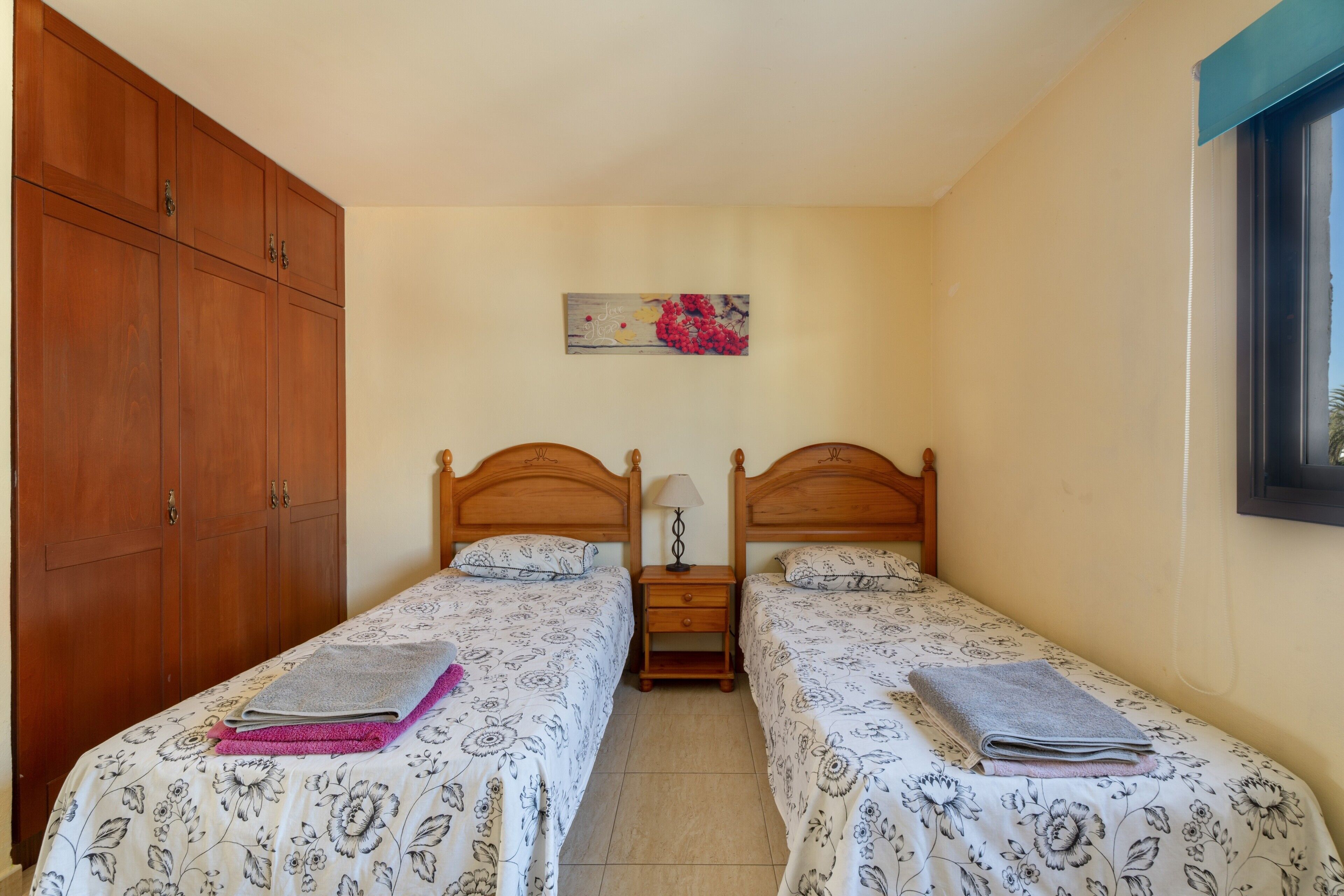 Une chambre avec deux lits simples, une armoire en bois, des tables de chevet et une œuvre d’art accrochée au mur.
