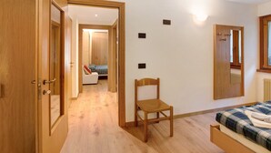 A bedroom with a wooden bed, a chair, a mirror, and a door leading to another room. - Apartment 'Vittoria Bilo' with Mountain View, Terraces & Wi-Fi (Valfurva)