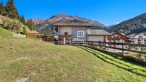 A mountain house with a wooden fence, a stone wall, and a view of the mountains. - Apartment 'Vittoria Bilo' with Mountain View, Terraces & Wi-Fi (Valfurva)