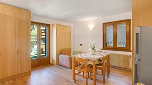 A room with a wooden floor, a dining table with chairs, a refrigerator, and a window with a wooden frame. - Apartment 'Vittoria Bilo' with Mountain View, Terraces & Wi-Fi (Valfurva)
