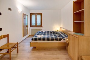 A bedroom with a wooden bed, a chair, a wardrobe, a window, and a radiator.