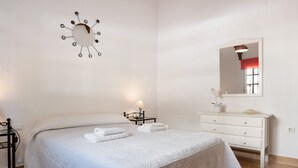 A bedroom with a bed, bedside table, lamp, dresser, and a wall clock. - Pet-Friendly 'Apartment en la Playa 2' with Terrace & Wi-Fi (Conil de la Frontera)