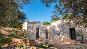 A stone building with a courtyard, featuring a stone wall, a cactus, and a potted plant.