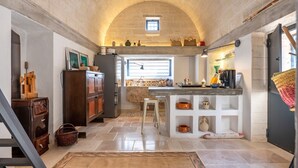 A kitchen with a stone arch ceiling, a wooden cabinet, a small window, and a white countertop with various kitchen items.