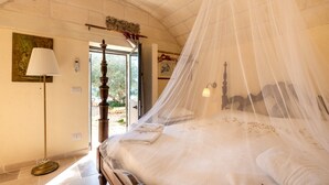 A bedroom with a four-poster bed, a standing lamp, and a view through an open door.