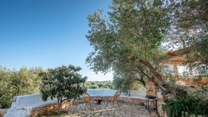 An outdoor patio with stone flooring, two wicker chairs, a small table, and a view of the countryside.