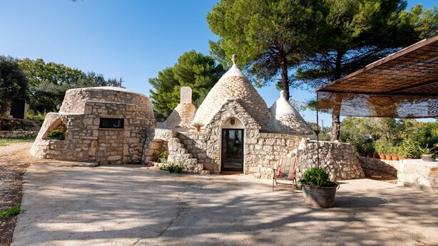 A stone building with a door, steps leading to it, and a bench with a potted plant. - Holiday Home Trullo with Shared Pool, Shared Garden & Terrace (Ostuni)