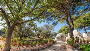 A stone pathway lined with potted plants leading to a rustic stone building with a dome roof. - Holiday Home Trullo with Shared Pool, Shared Garden & Terrace (Ostuni)