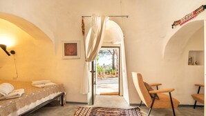 A room with a bed, a chair, a rug, and a view through an open doorway. - Holiday Home Trullo with Shared Pool, Shared Garden & Terrace (Ostuni)