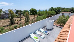 Terrassa al terrat amb gandules, una columna blanca gran i vistes al mar i al verd.