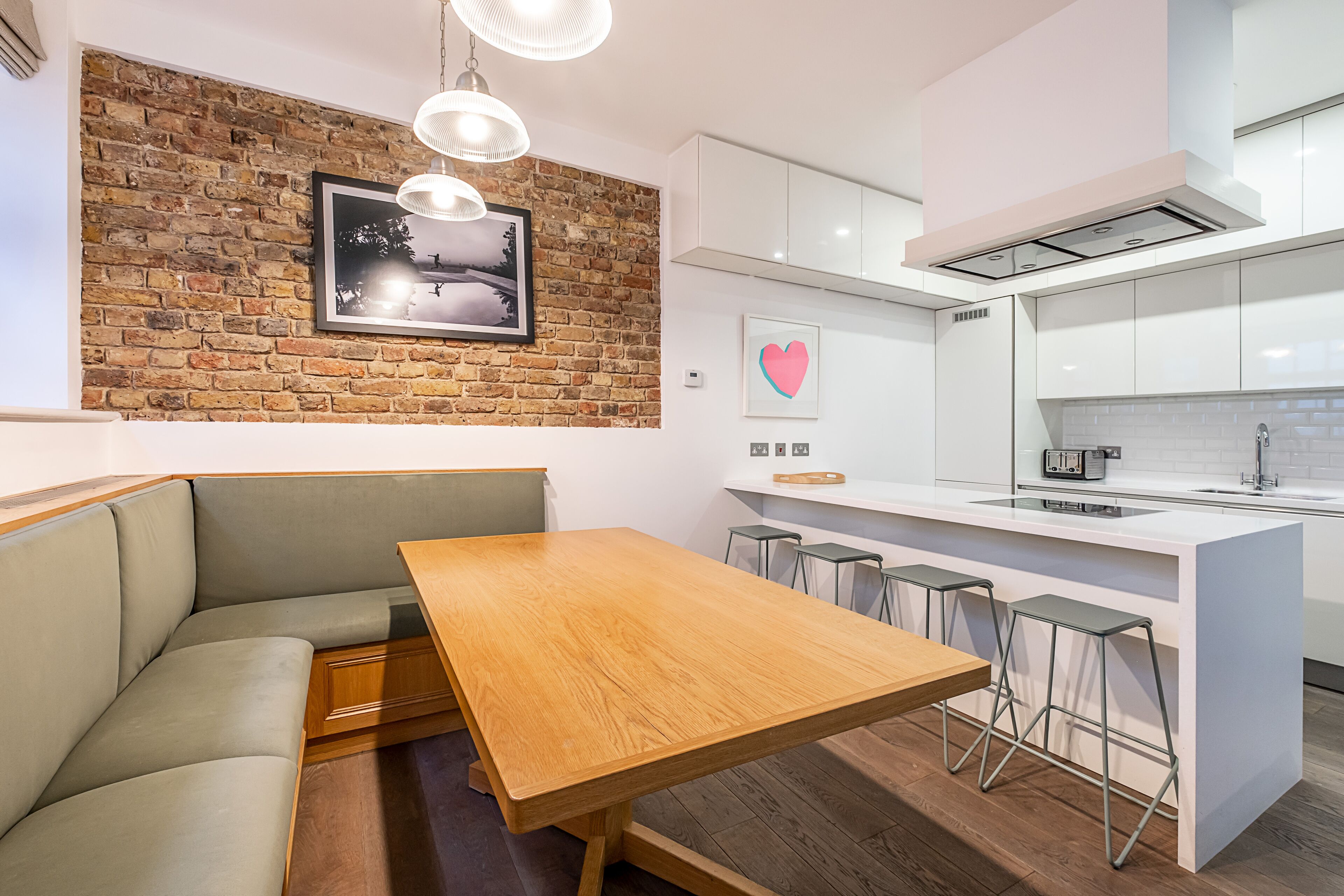 Une cuisine moderne avec une table à manger en bois, des tabourets de bar et un mur d’accent en briques.