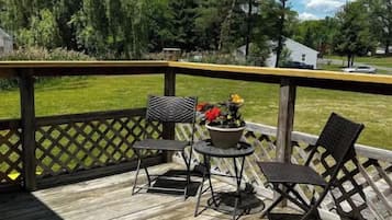 Eine Holzterrasse mit Gittergeländer, zwei Metallstühlen, einem kleinen runden Tisch und einem Blumentopf.