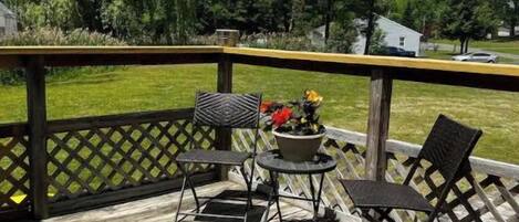 A wooden deck with a lattice railing, two metal chairs, a small round table, and a potted plant.