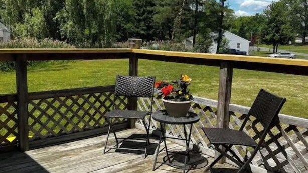 Eine Holzterrasse mit Gittergeländer, zwei Metallstühlen, einem kleinen runden Tisch und einem Blumentopf.