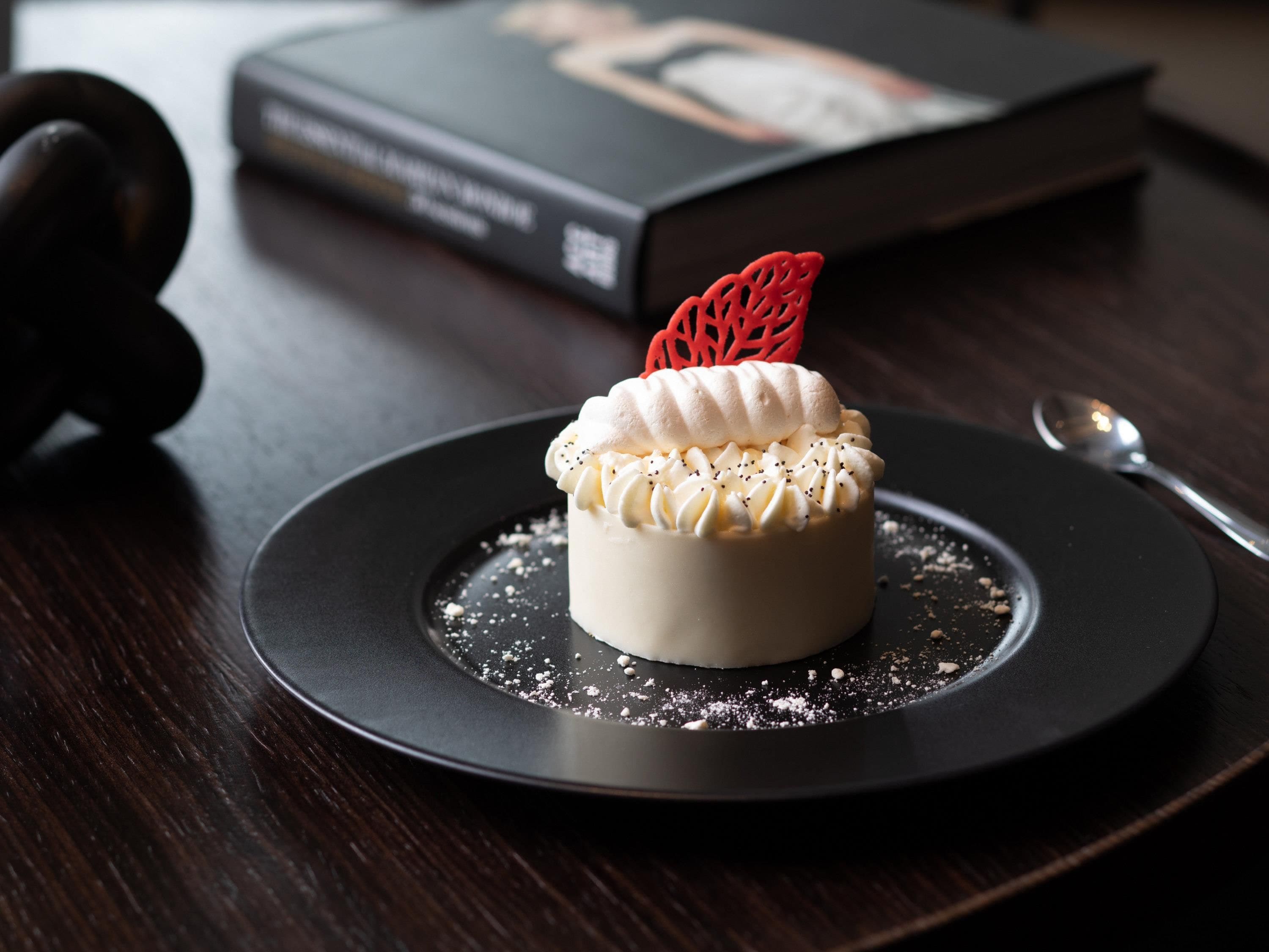 A dessert on a black plate with a book and a spoon in the background.
