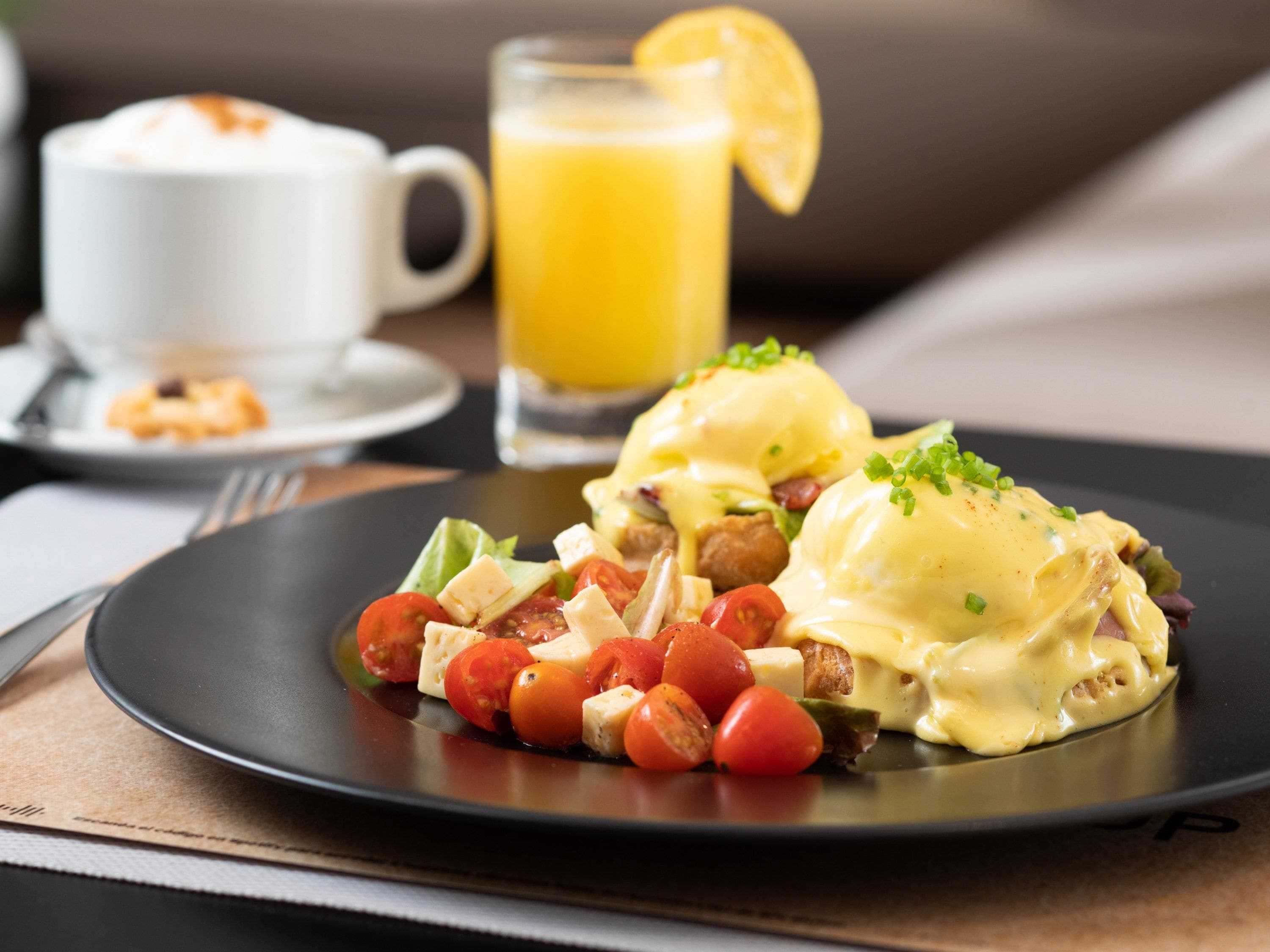 Une assiette de petit-déjeuner avec des œufs Bénédicte, des tomates cerises et un verre de jus d’orange.