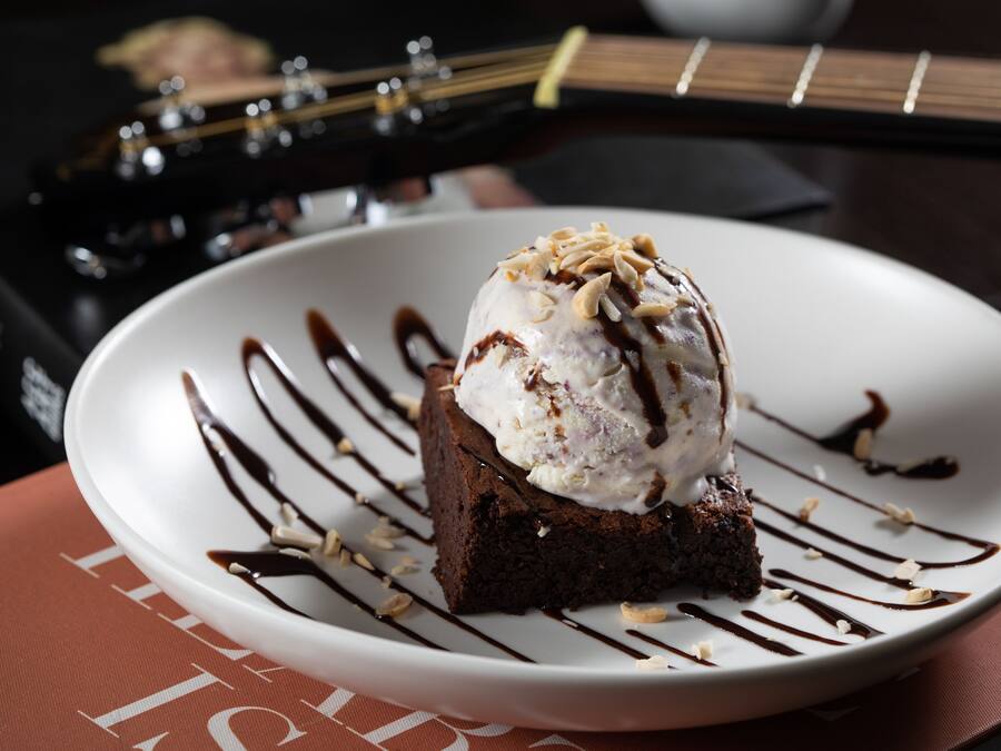 Un dessert servi dans une assiette, nappé de sauce au chocolat et agrémenté de noix, avec une guitare en arrière-plan.
