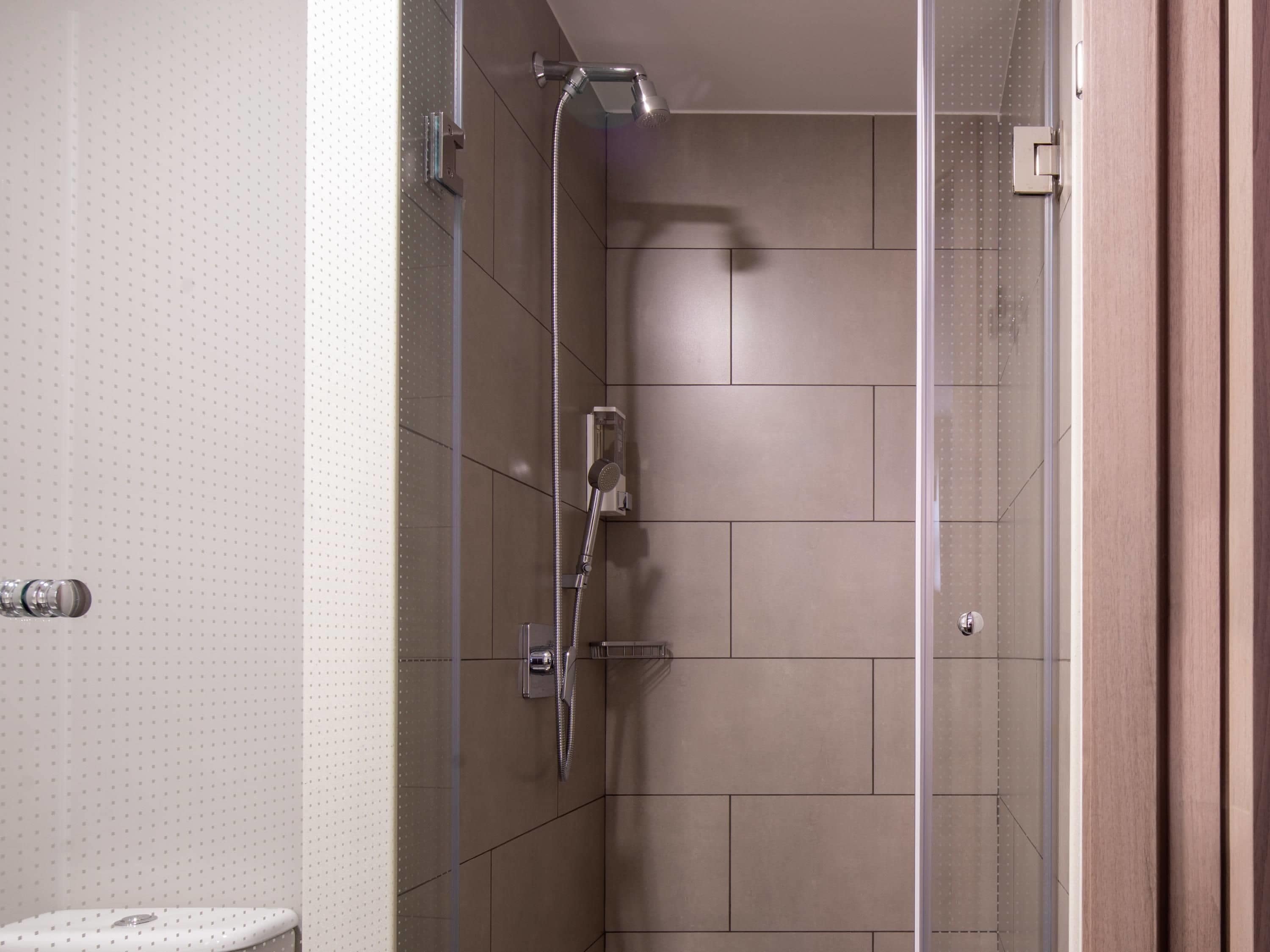 Una ducha moderna con puerta de vidrio, cabezal de ducha de mano y llave de pared.