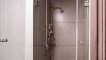 A modern shower with a glass door, a handheld showerhead, and a wall-mounted faucet.