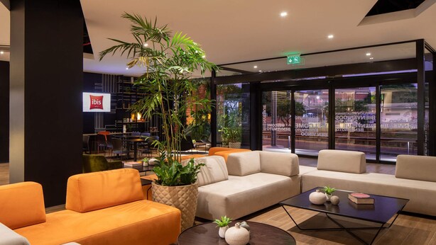 Un hall d’entrée moderne avec des coins salon, une table basse et une grande plante en pot.