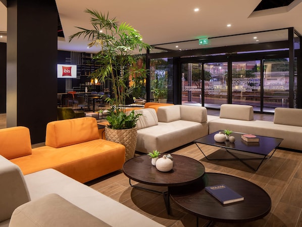 A modern lobby with seating areas, a coffee table, and a large potted plant.