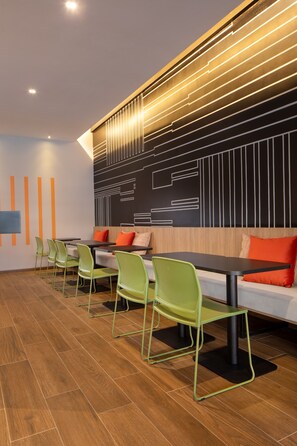 Un espace repas moderne avec des chaises vertes, une longue table et un mur orné de motifs géométriques.