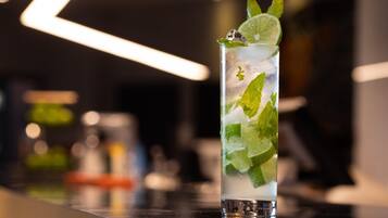 A tall glass with a lime slice and mint leaves, filled with ice and a clear liquid, placed on a reflective surface.