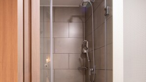 Une douche moderne avec une porte en verre, des murs carrelés et des toilettes visibles dans la salle de bain adjacente.