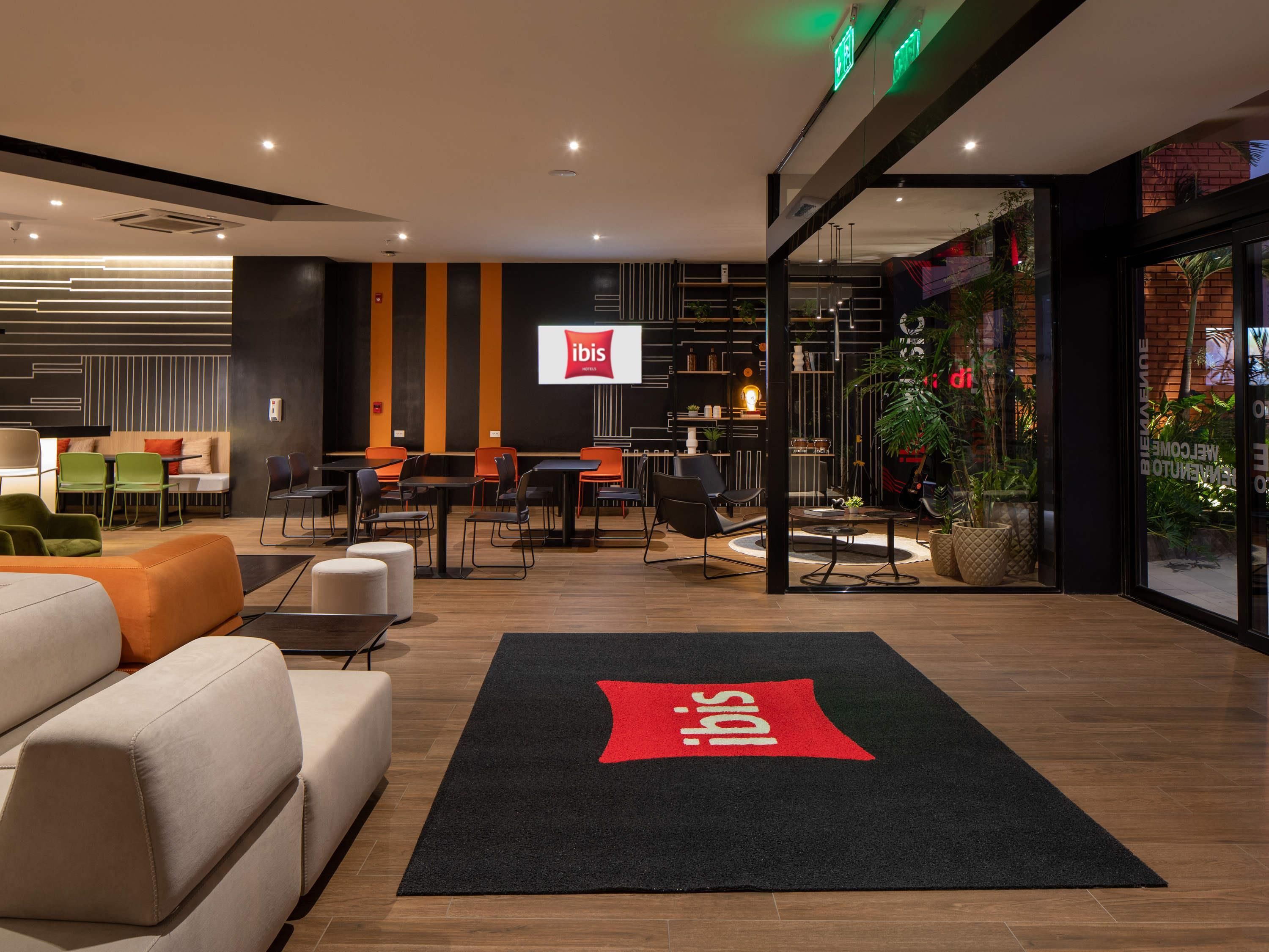 Un moderno vestíbulo de hotel con zonas de estar, un mostrador de recepción y un amplio ventanal con plantas.
