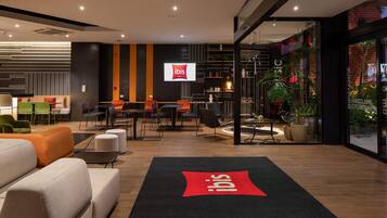 Un moderno vestíbulo de hotel con zonas de estar, un mostrador de recepción y un amplio ventanal con plantas.