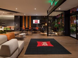 Un moderno vestíbulo de hotel con zonas de estar, un mostrador de recepción y un amplio ventanal con plantas.
