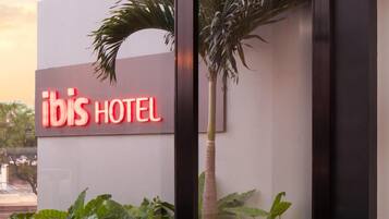 An ibis hotel sign with outdoor seating and a palm tree.